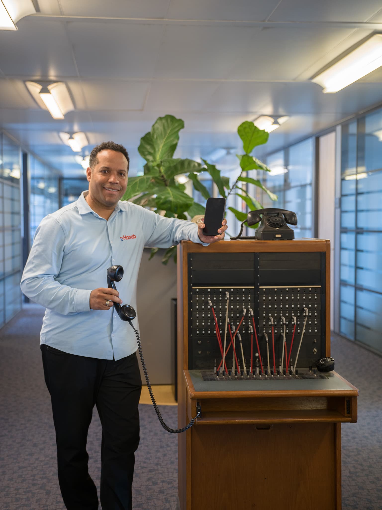 Hanab medewerker met vintage telefooncentrale en smartphone symboliseert historie en innovatie