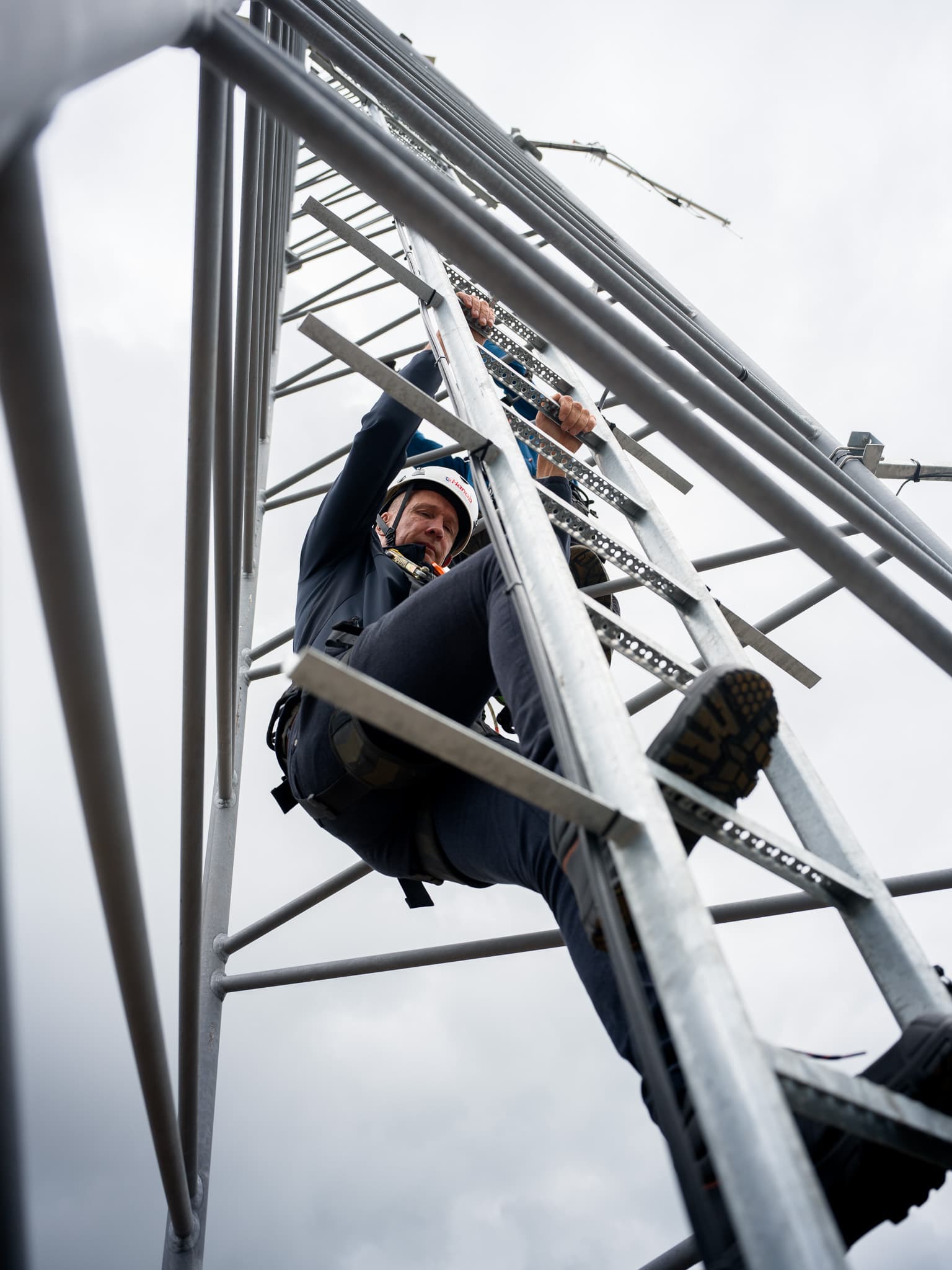 Monteur hangt in klimgordel hoog in stalen vakwerkmast tijdens onderhoudswerkzaamheden