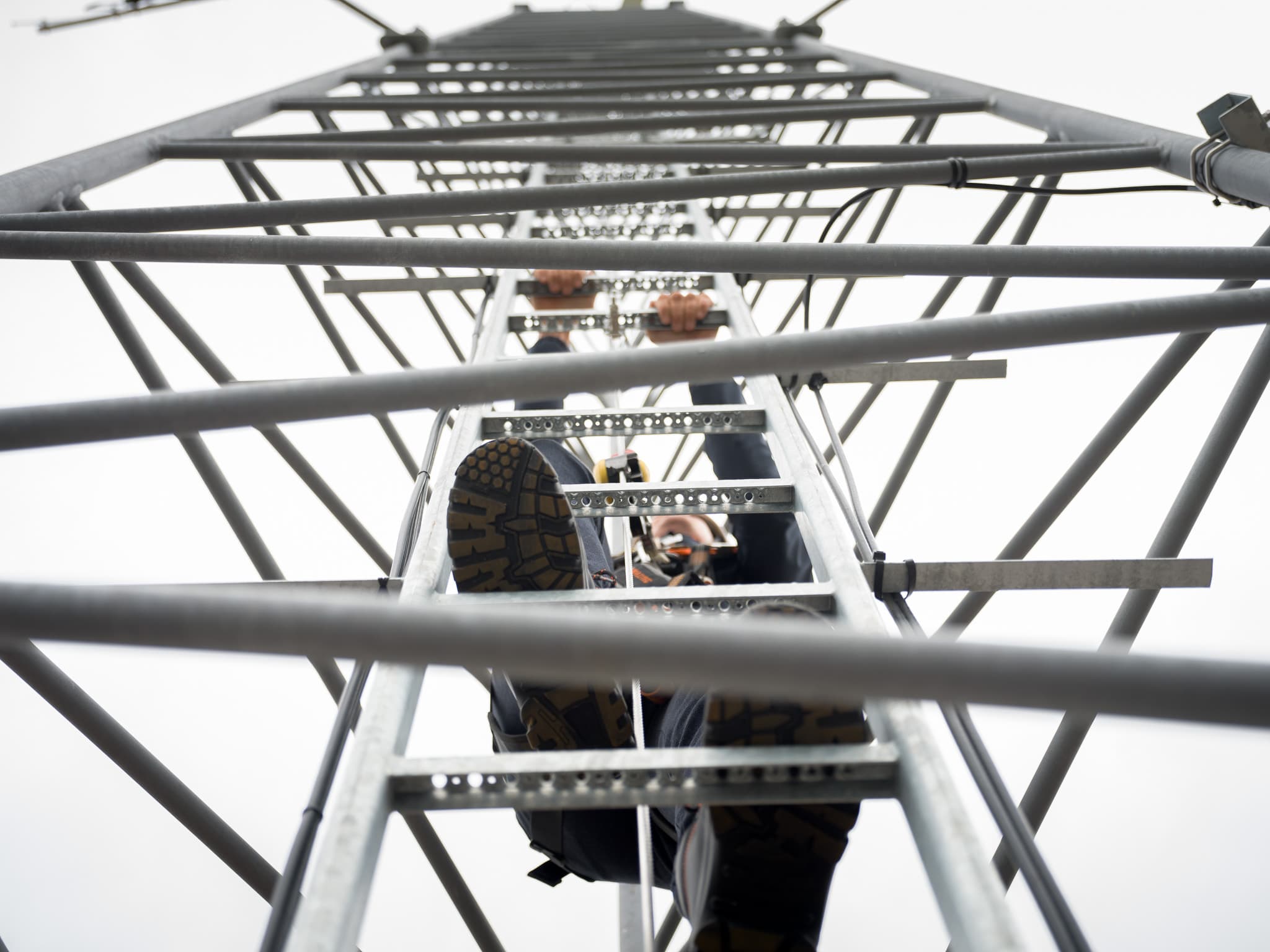 Laag camerastandpunt vanuit de mast toont monteur die traliewerk beklimt richting antennes