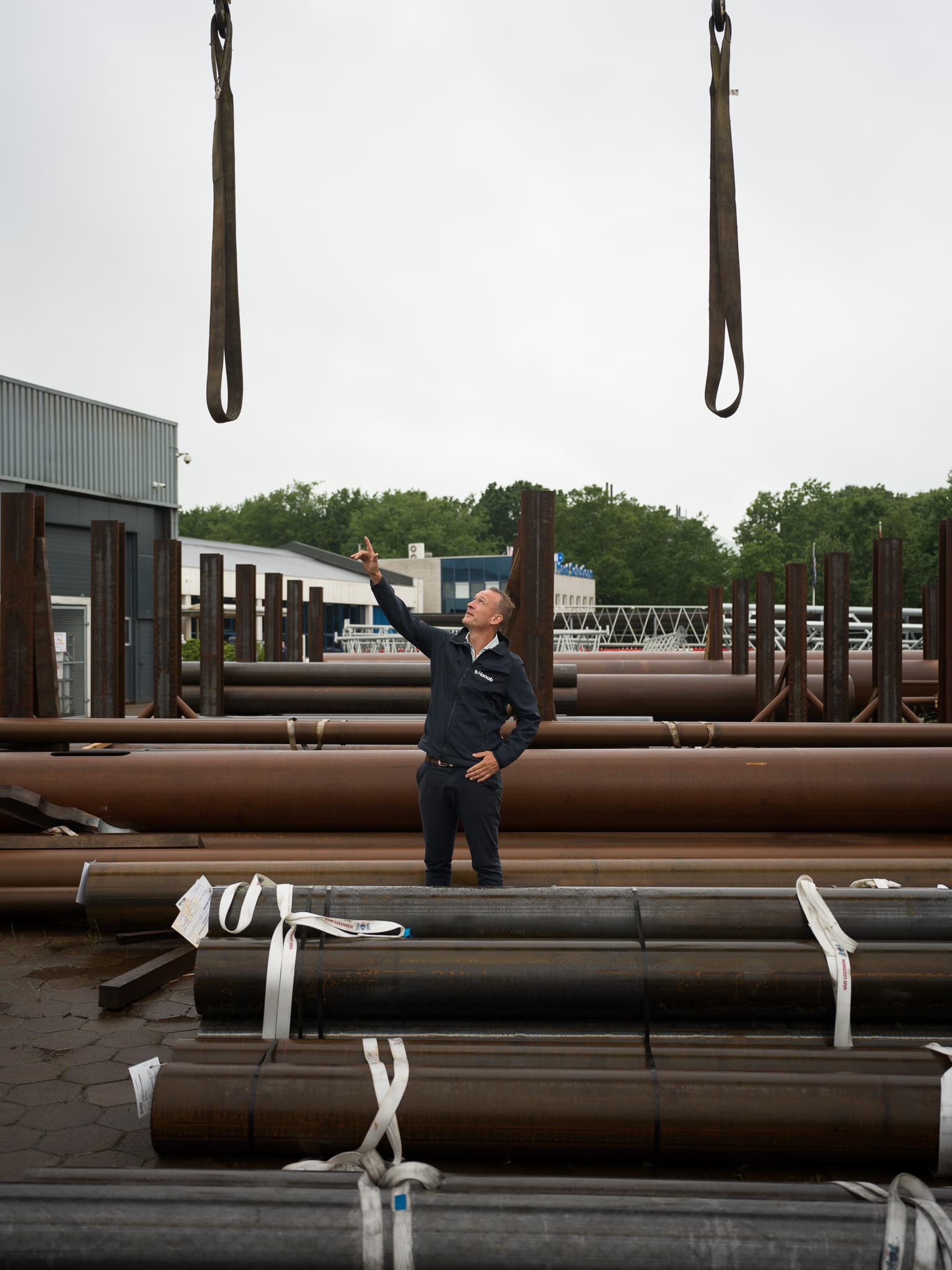 Hanab medewerker wijst omhoog tussen opgeslagen stalen buizen en mastonderdelen op buitenterrein