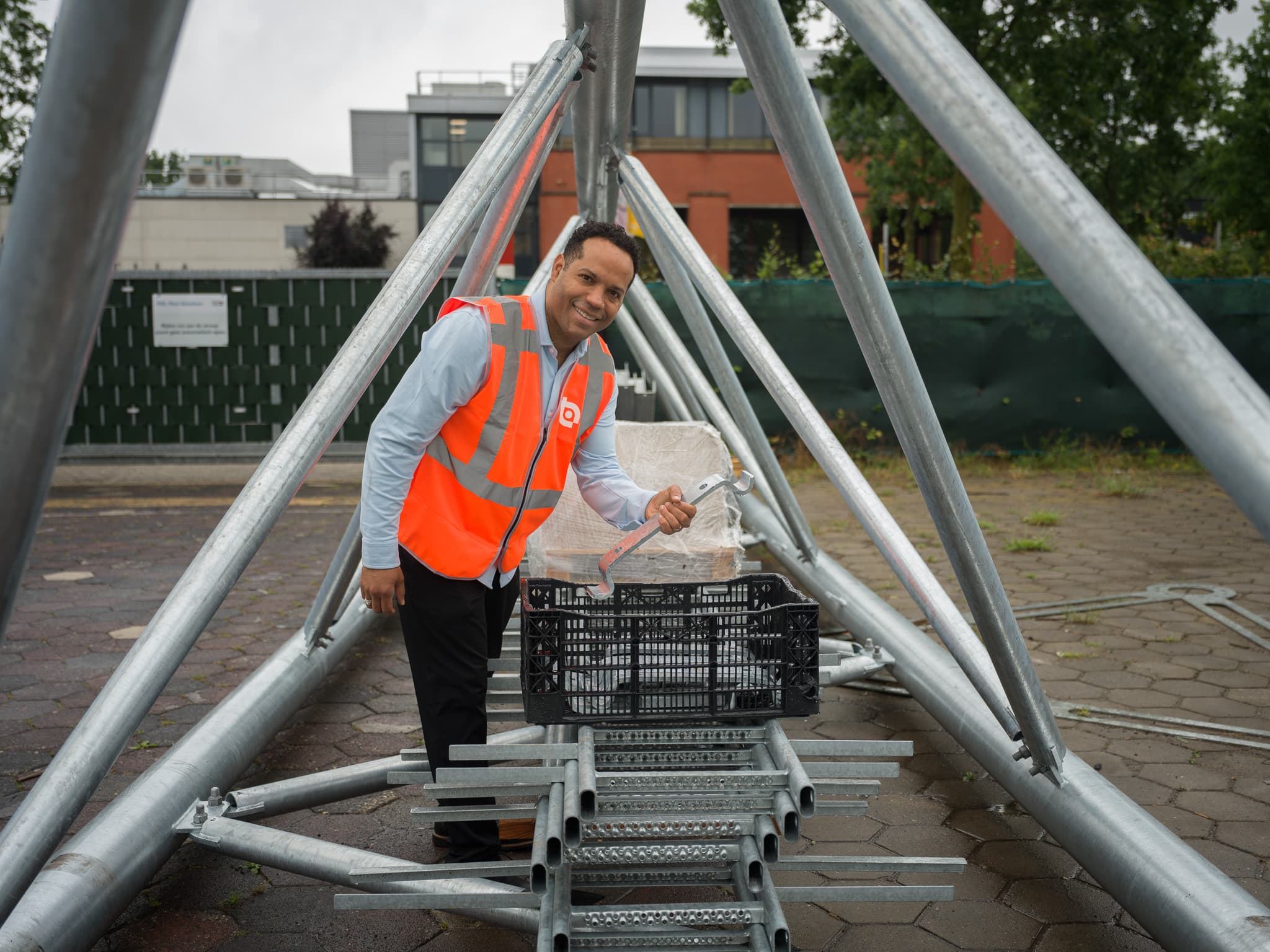 Man in veiligheidsvest met moersleutel bij fundering van stalen mastconstructie op straat
