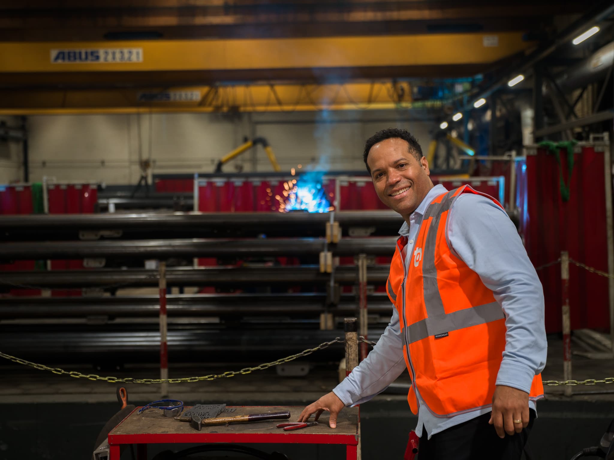 Glimlachende medewerker bij lasproces met vonken op de achtergrond in de staalfabriek