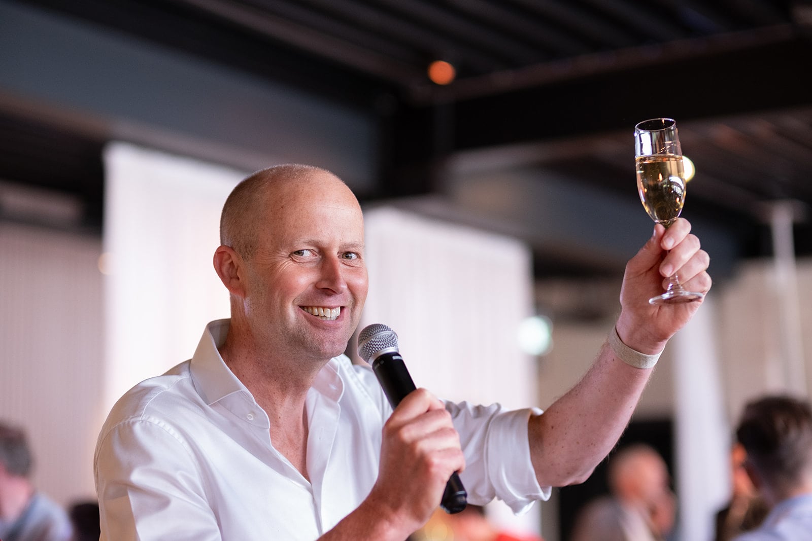 Lachende man met microfoon houdt champagne toast tijdens bedrijfsfeest