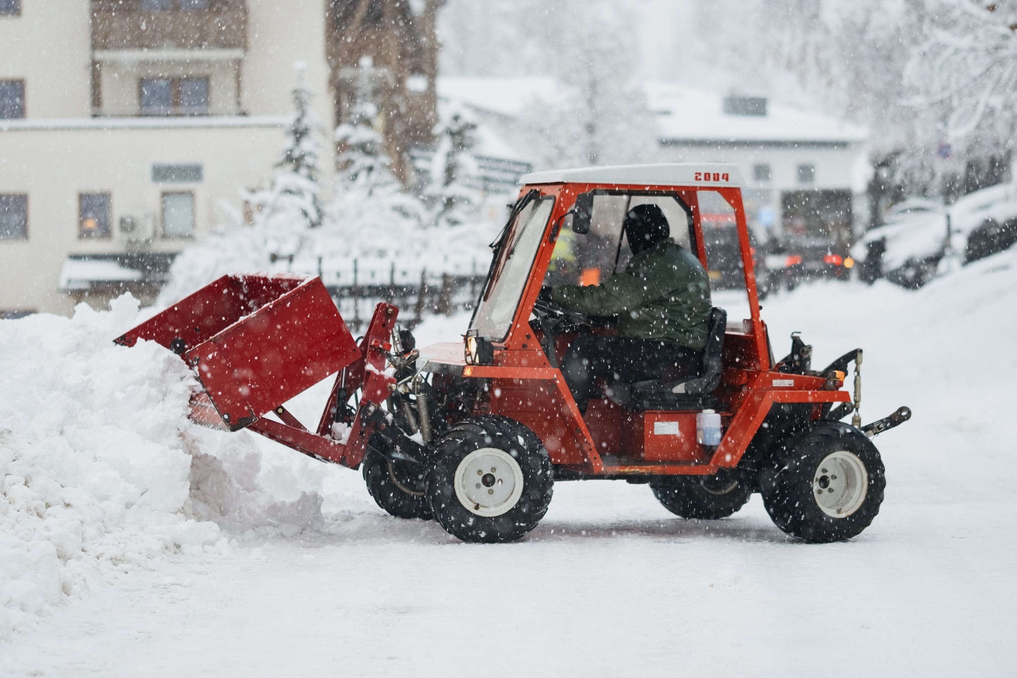 Rode sneeuwschuiver werkt tijdens sneeuwval in skiplaats - winterse dorpsfeer