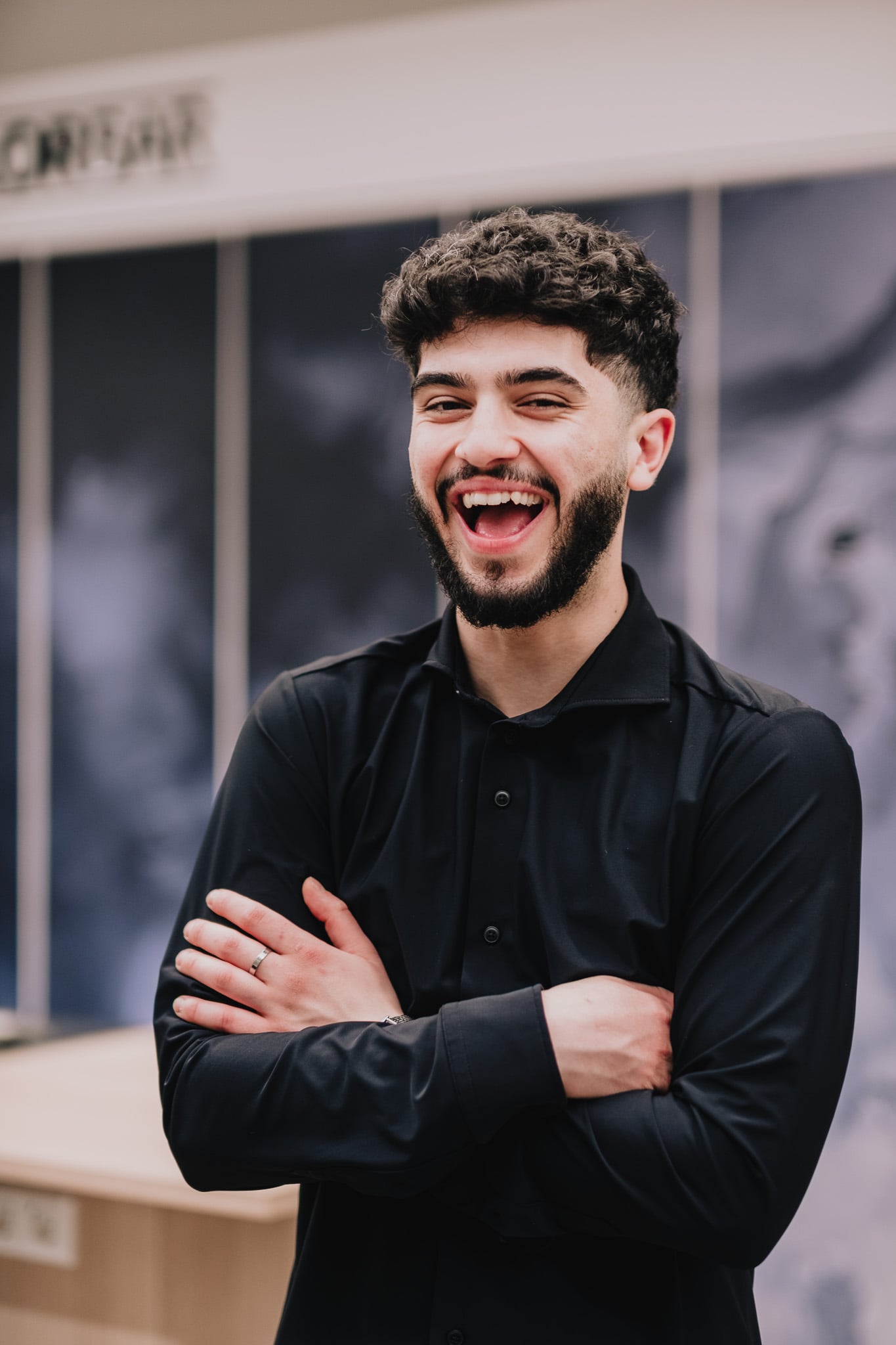 Vrolijke kapper met krullend haar en baard lacht hartelijk met gekruiste armen, spontaan teamportret