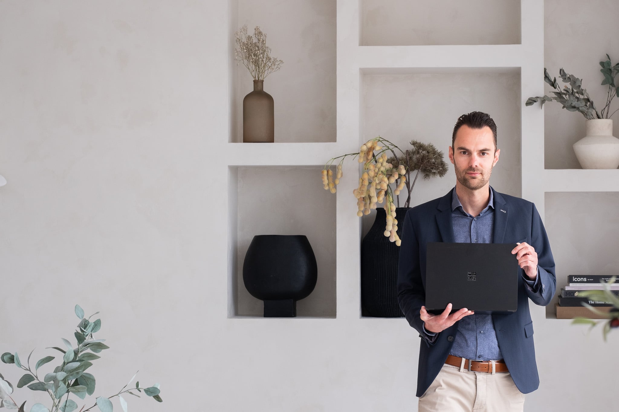 Business portret man in colbert met Surface laptop in stijlvol interieur met vazen
