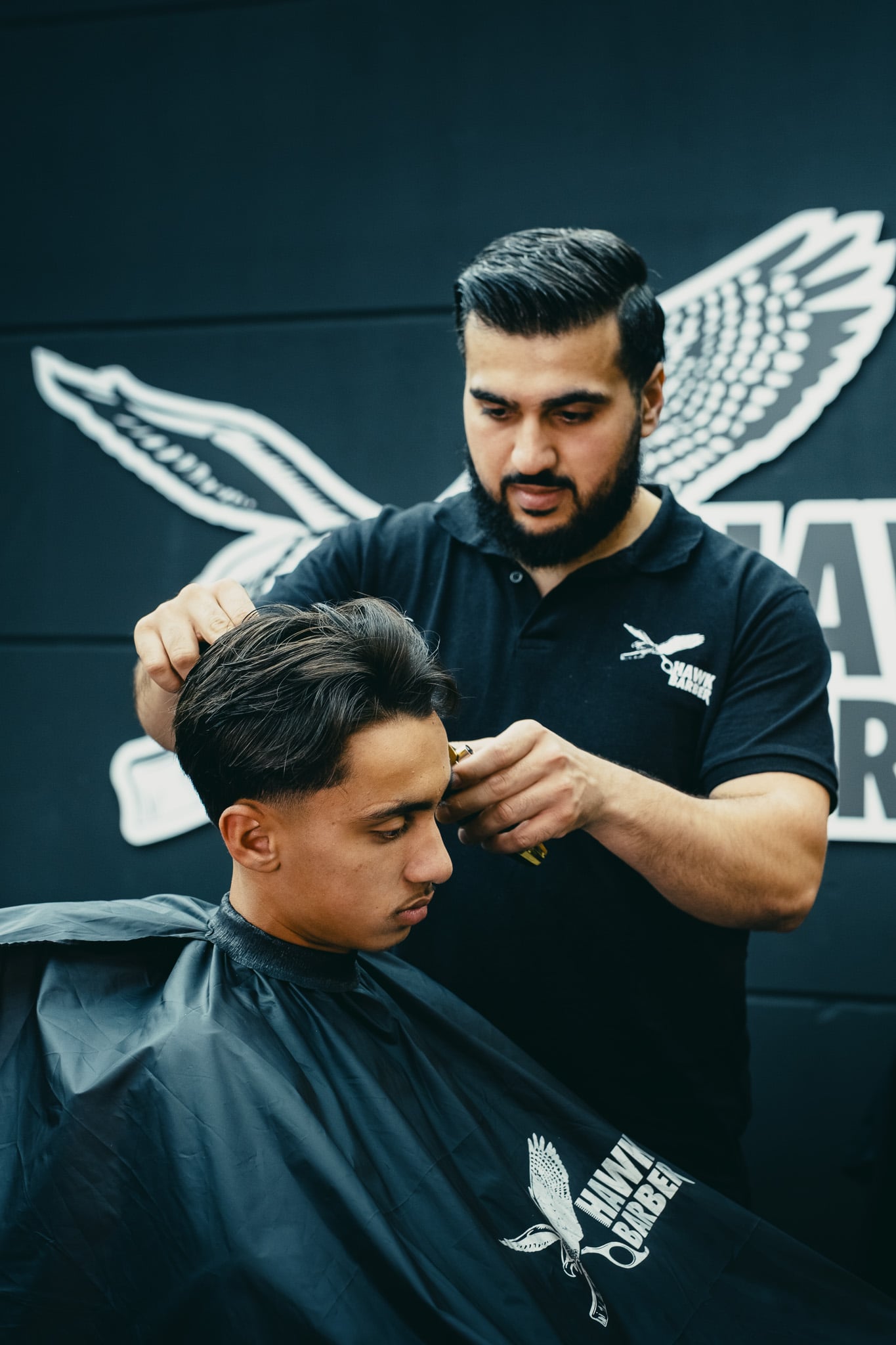 Geconcentreerde barbier knipt donker haar van klant voor grote Hawk Barber muurschildering