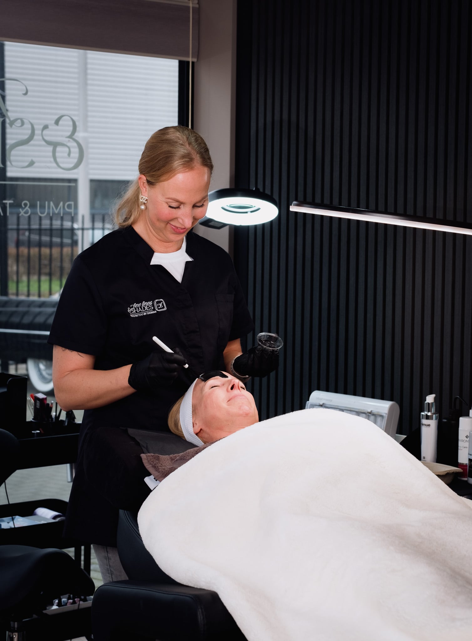 Schoonheidsspecialiste Fine Lines & Shades behandelt klant met gezichtsbehandeling onder professionele studiolamp