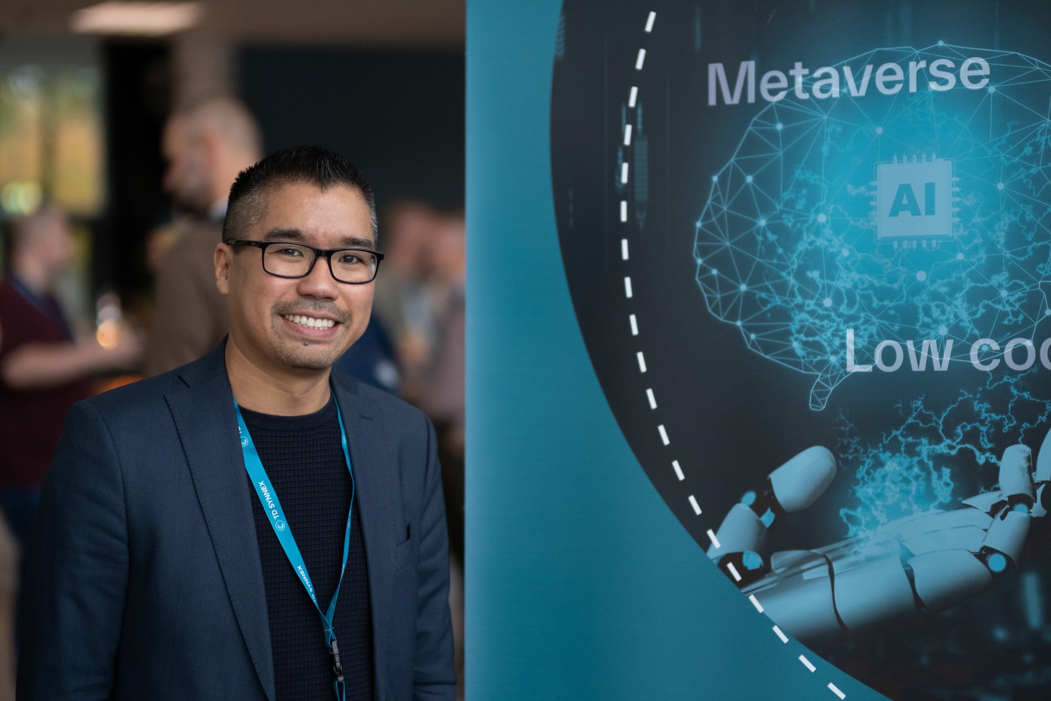Lachende Aziatische man in donkerblauw pak naast Metaverse AI technologie display op beurs