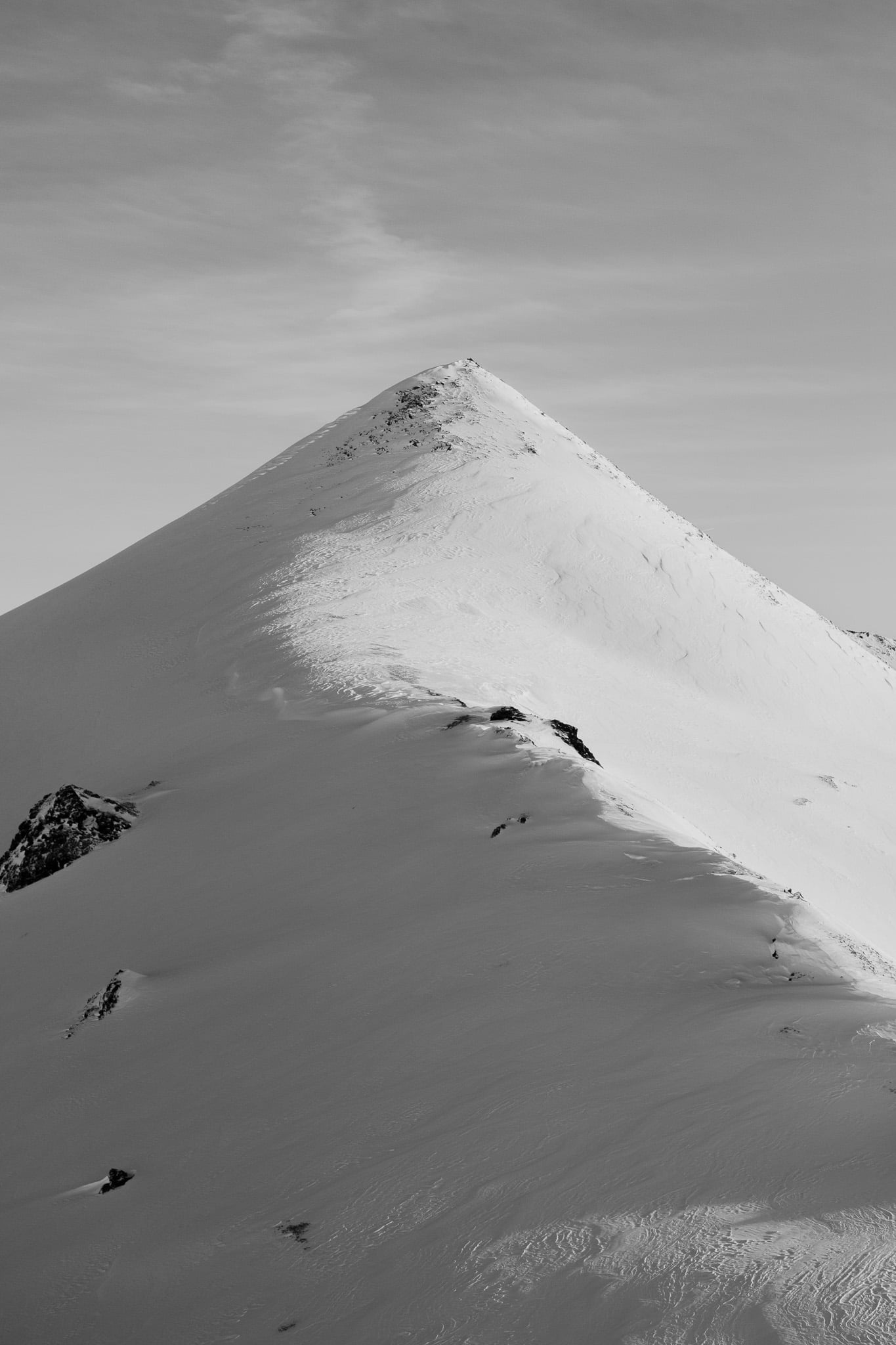 Geïsoleerde bergpiek met windgedreven sneeuwrichels - sculpturale Alpine topografie