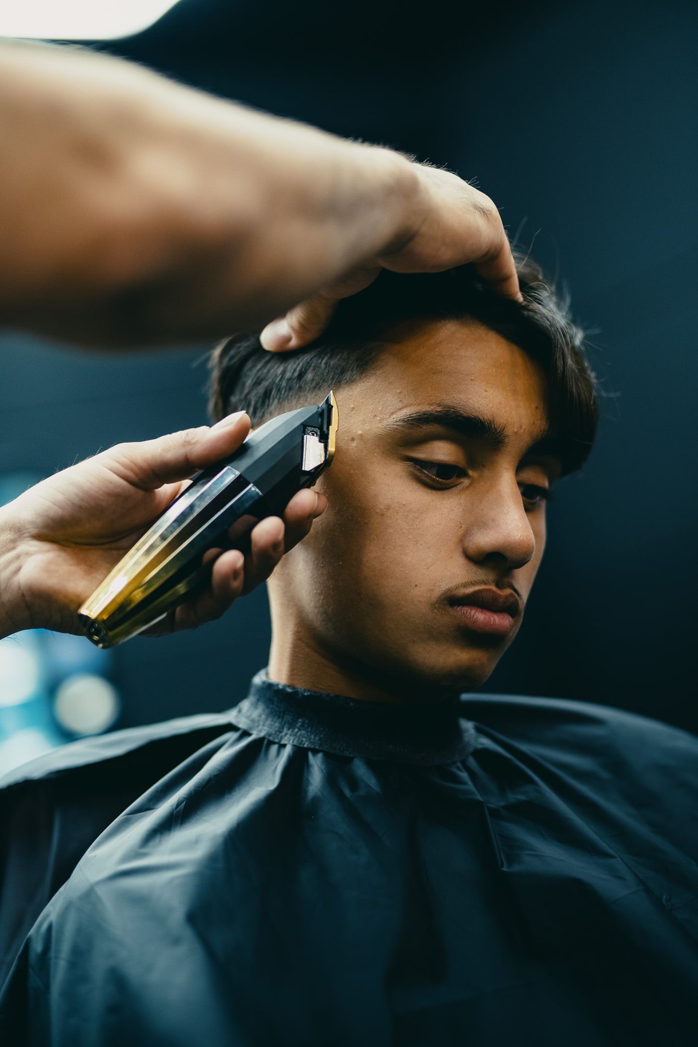 Close-up van haartrimmer tegen gezicht jonge man tijdens professionele knipbeurt in barbershop