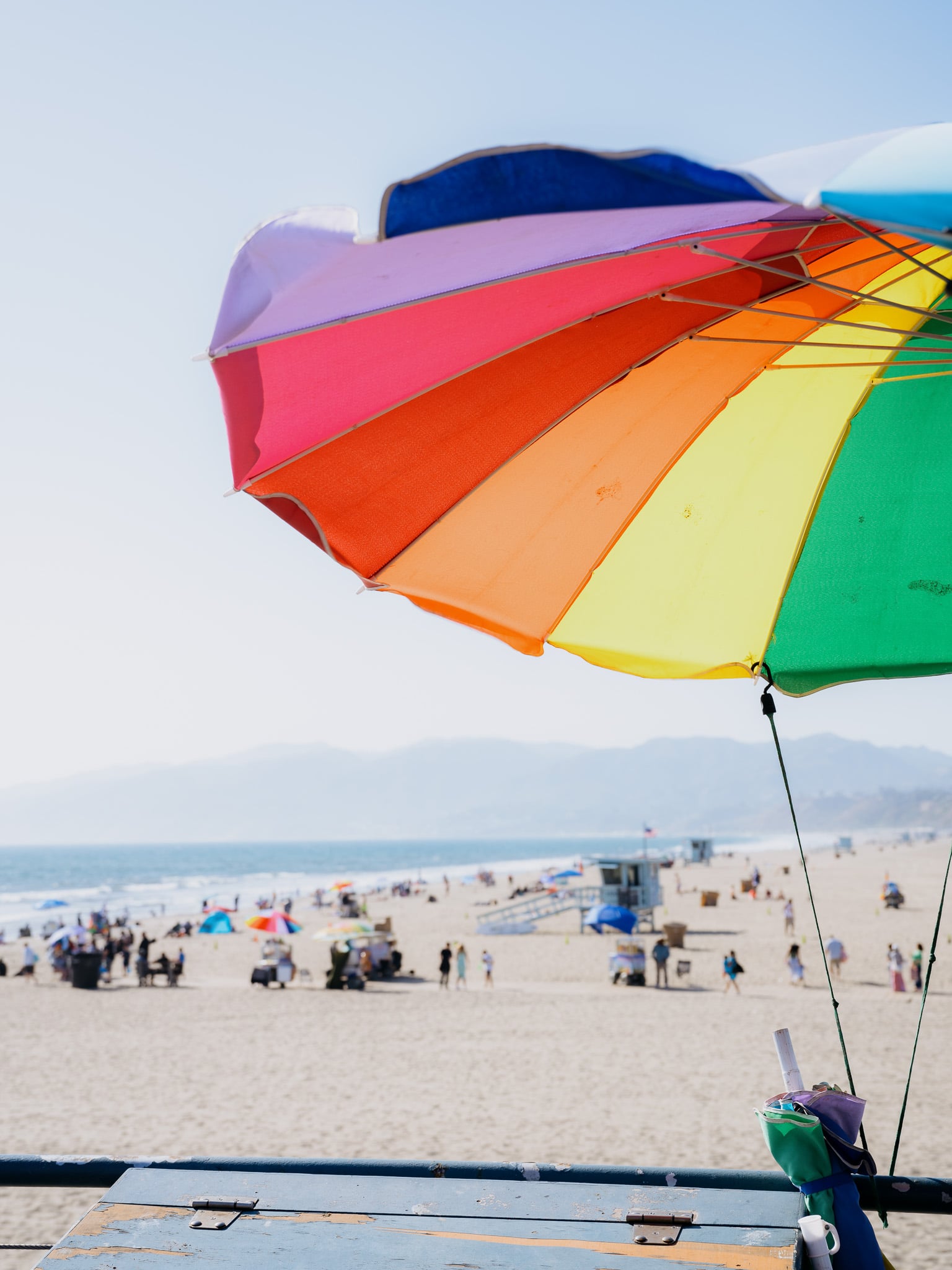 Kleurrijke strandparasol op Santa Monica Beach met zicht op zee, badmeestertoren en bergen op de achtergrond