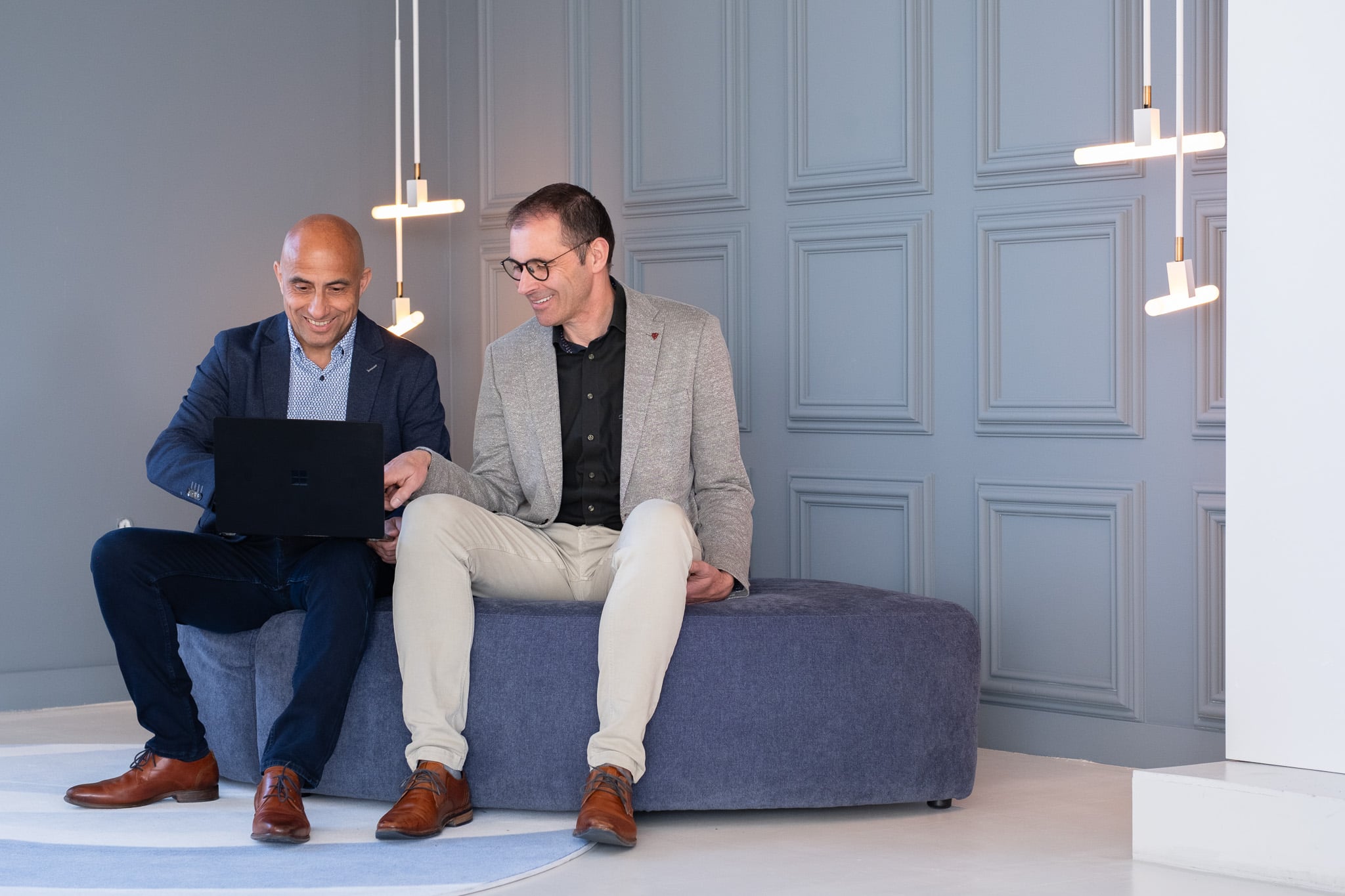 Zakenlieden lachen samen op bank met laptop moderne kantoorsfeer bedrijfsfotograaf Utrecht