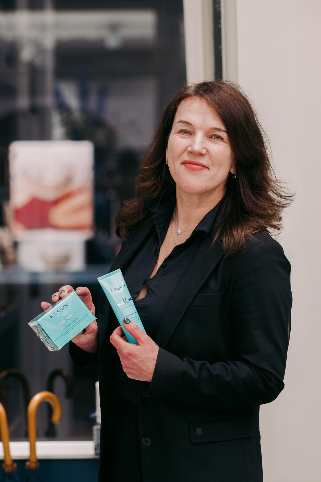 Professionele vrouw in zwarte blazer toont haarverzorgingsproducten, product presentatie kapsalon fotografie