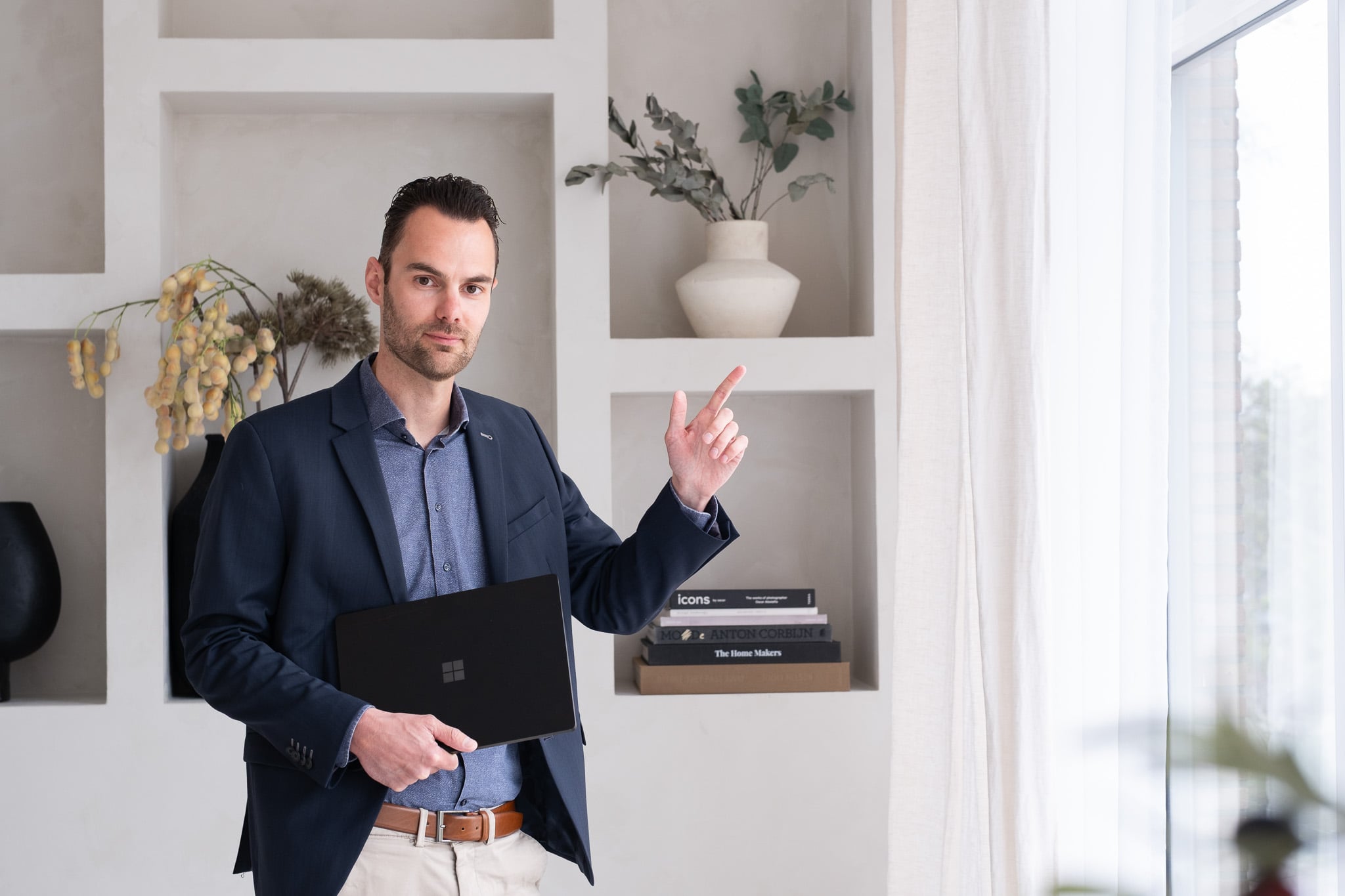 Professionele zakenman in donkerblauwe pak met laptop wijzend in moderne studio omgeving