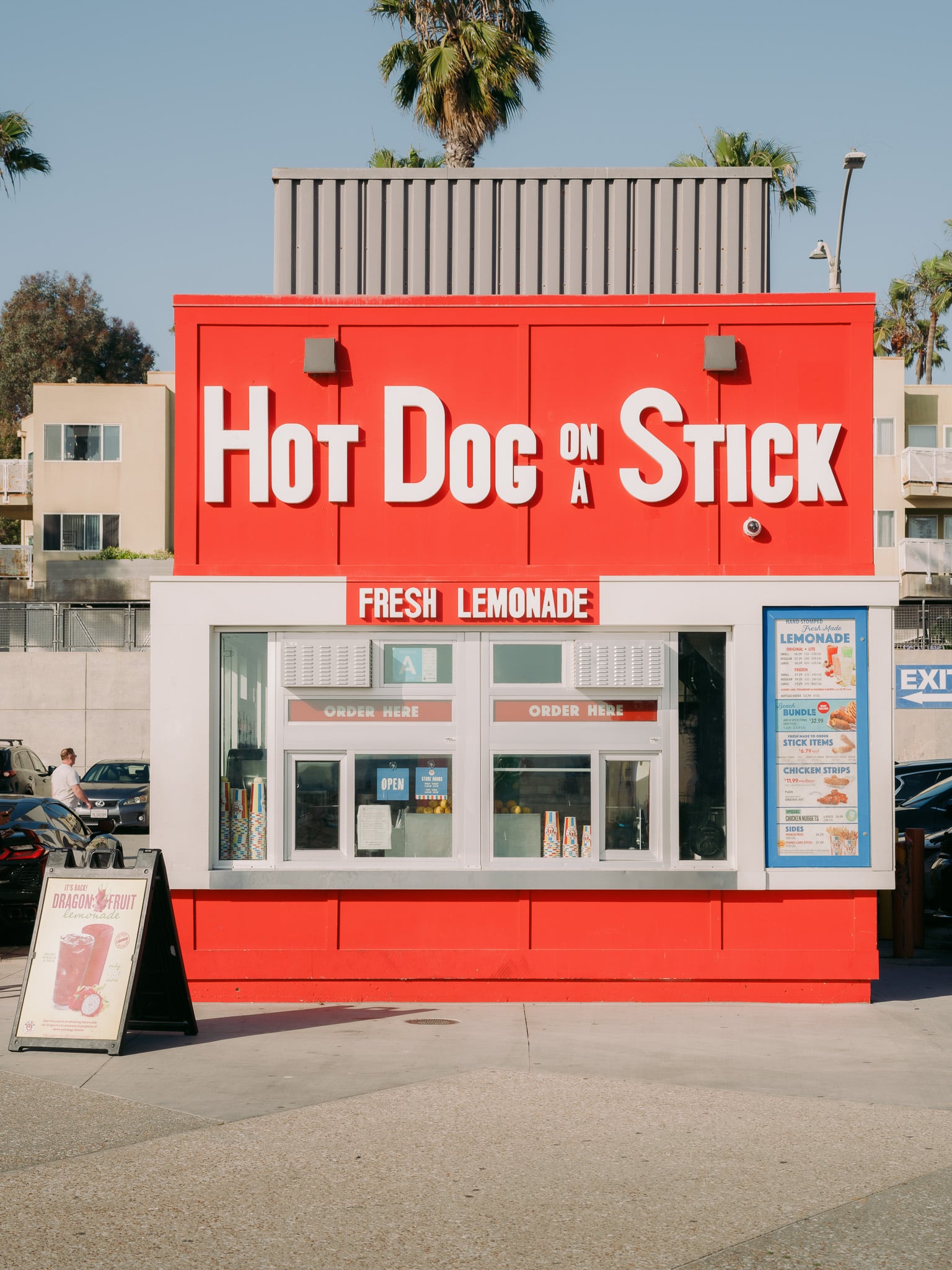 Rode gevel van Hot Dog on a Stick met palmboom en reclamebord voor dragonfruit limonade
