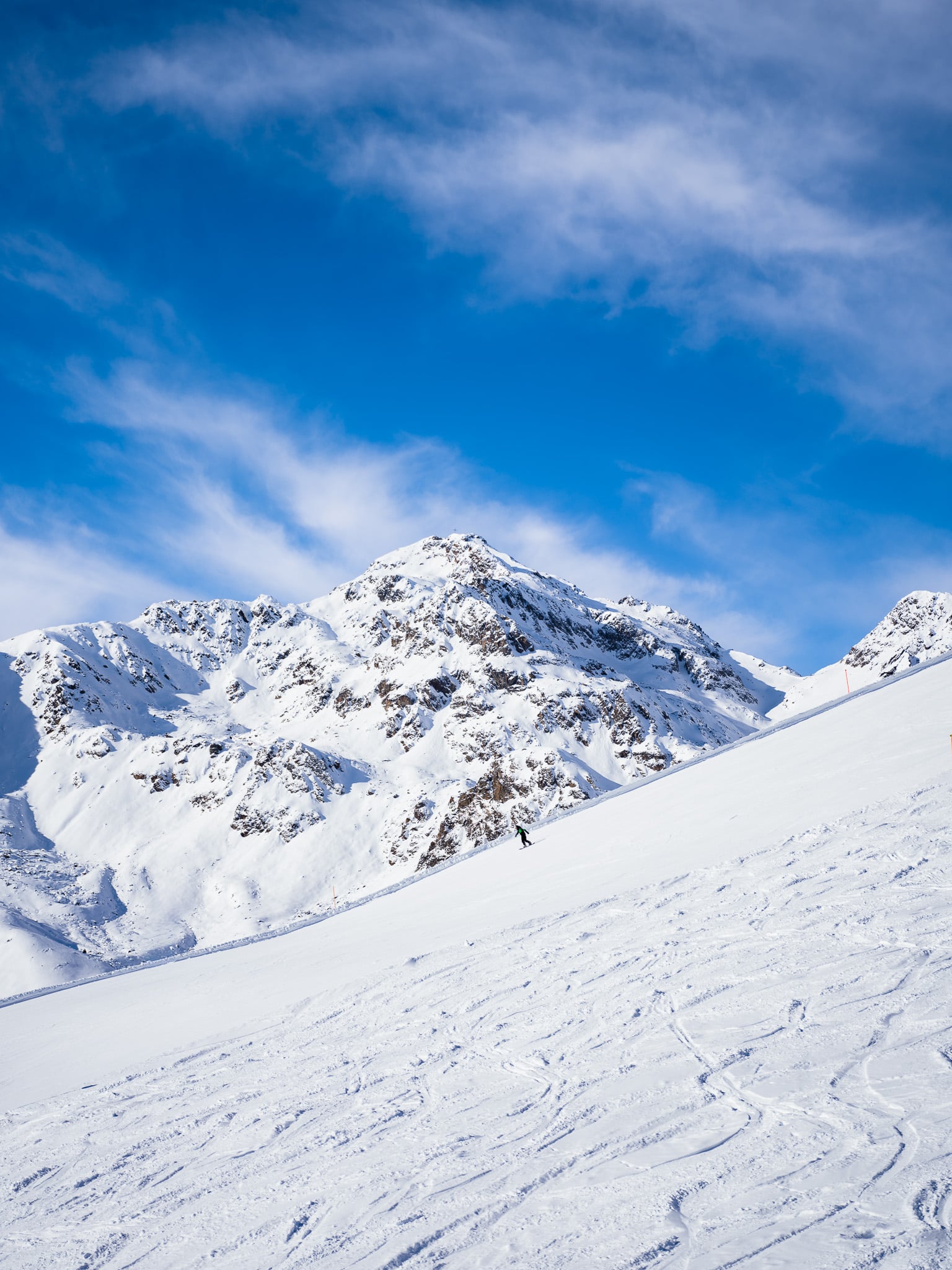 Eenzame figuur op uitgestrekte skipiste met bergketen - minimalistische bergfotografie