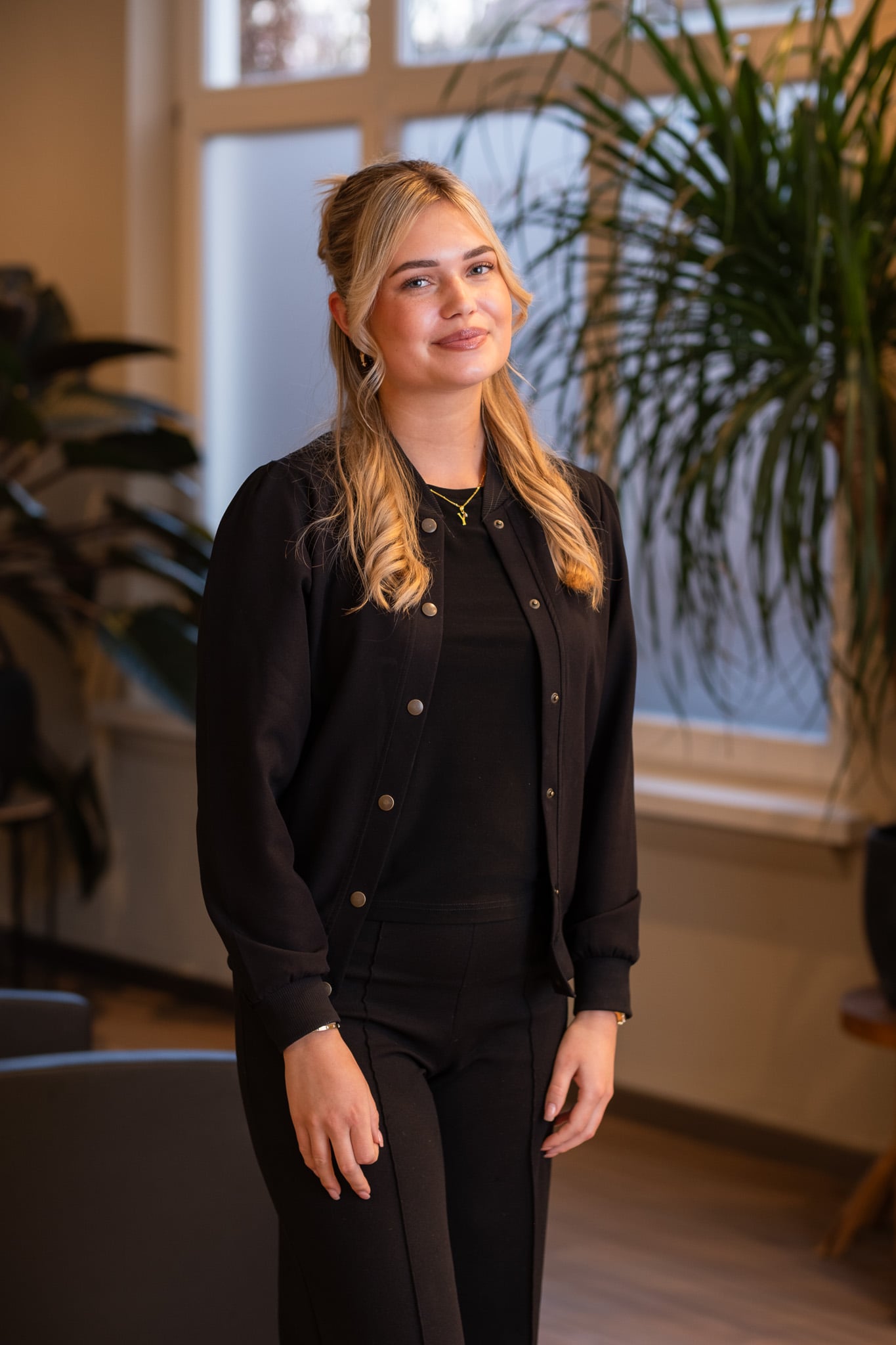 Kapster met opgestoken blonde haar kijkt over schouder in moderne kapsalon, natuurlijk licht portretfotografie