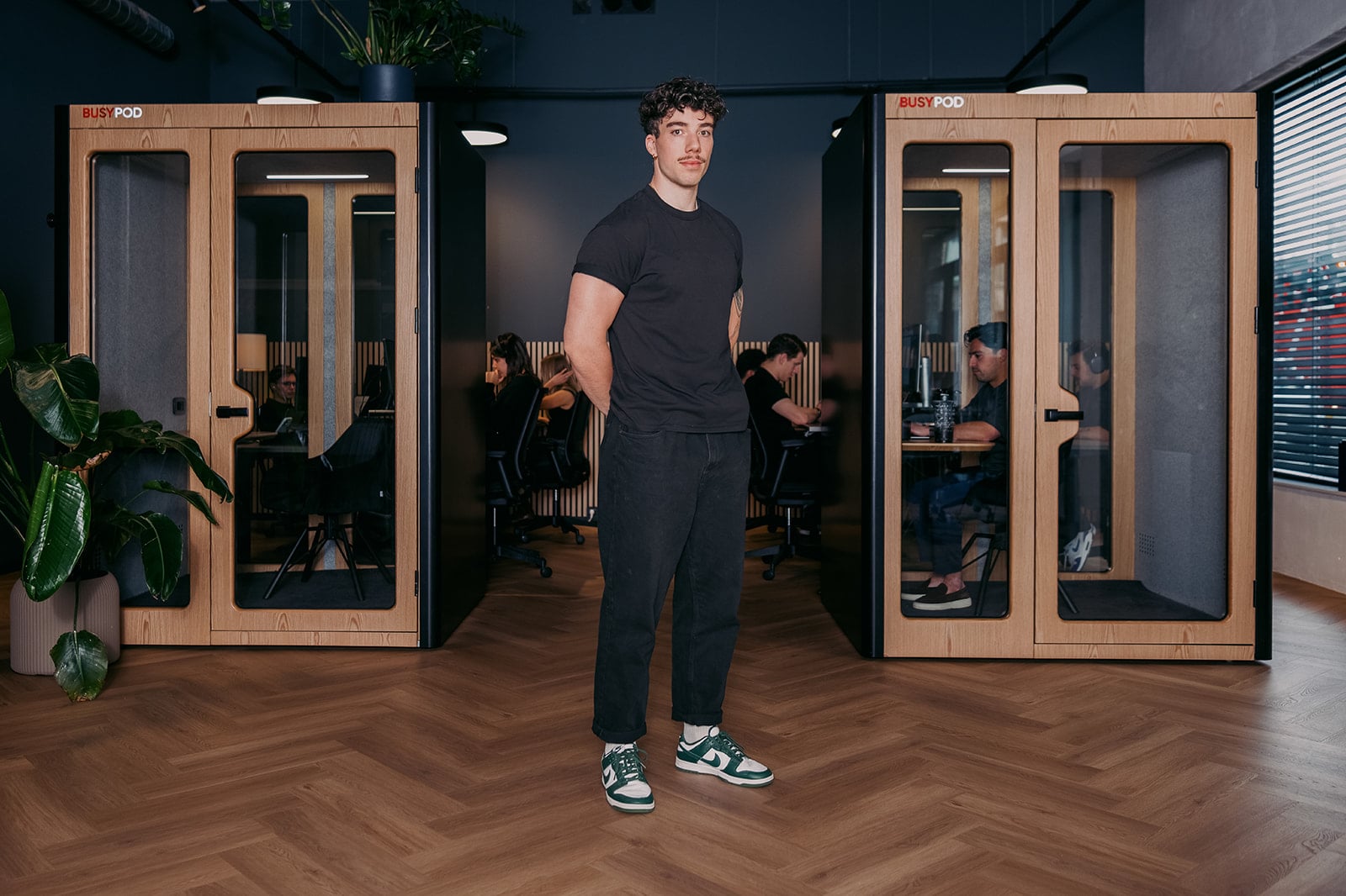 Jonge man zwart t-shirt jeans groene sneakers bedrijfsportret moderne kantoorinrichting Utrecht