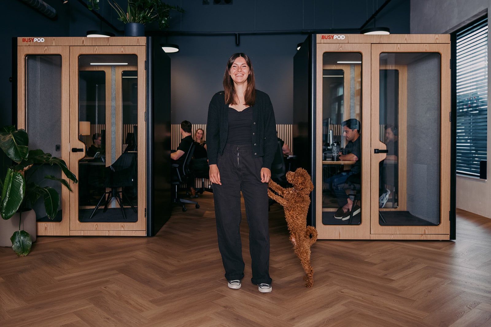 Vrolijke vrouw donkere kleding bruine hond op been kantoor busypod vergaderruimtes bedrijfsreportage