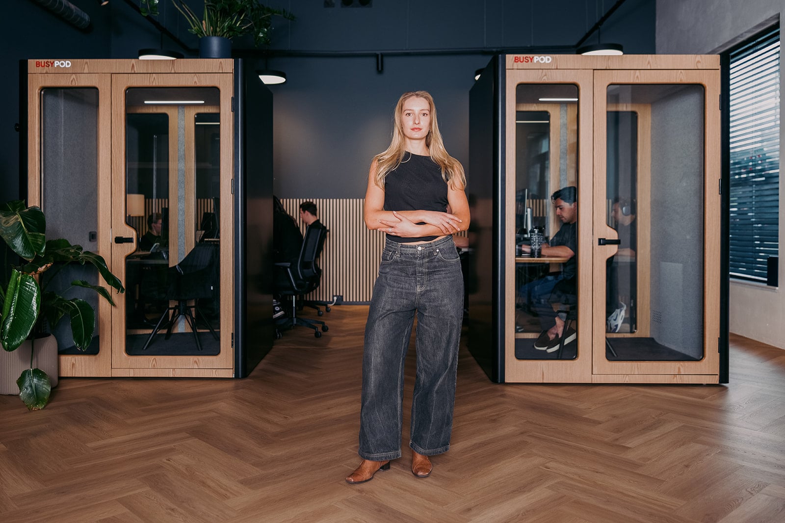 Blonde vrouw zwart shirt wijde jeans bruine schoenen professionele bedrijfsfotografie kantooromgeving