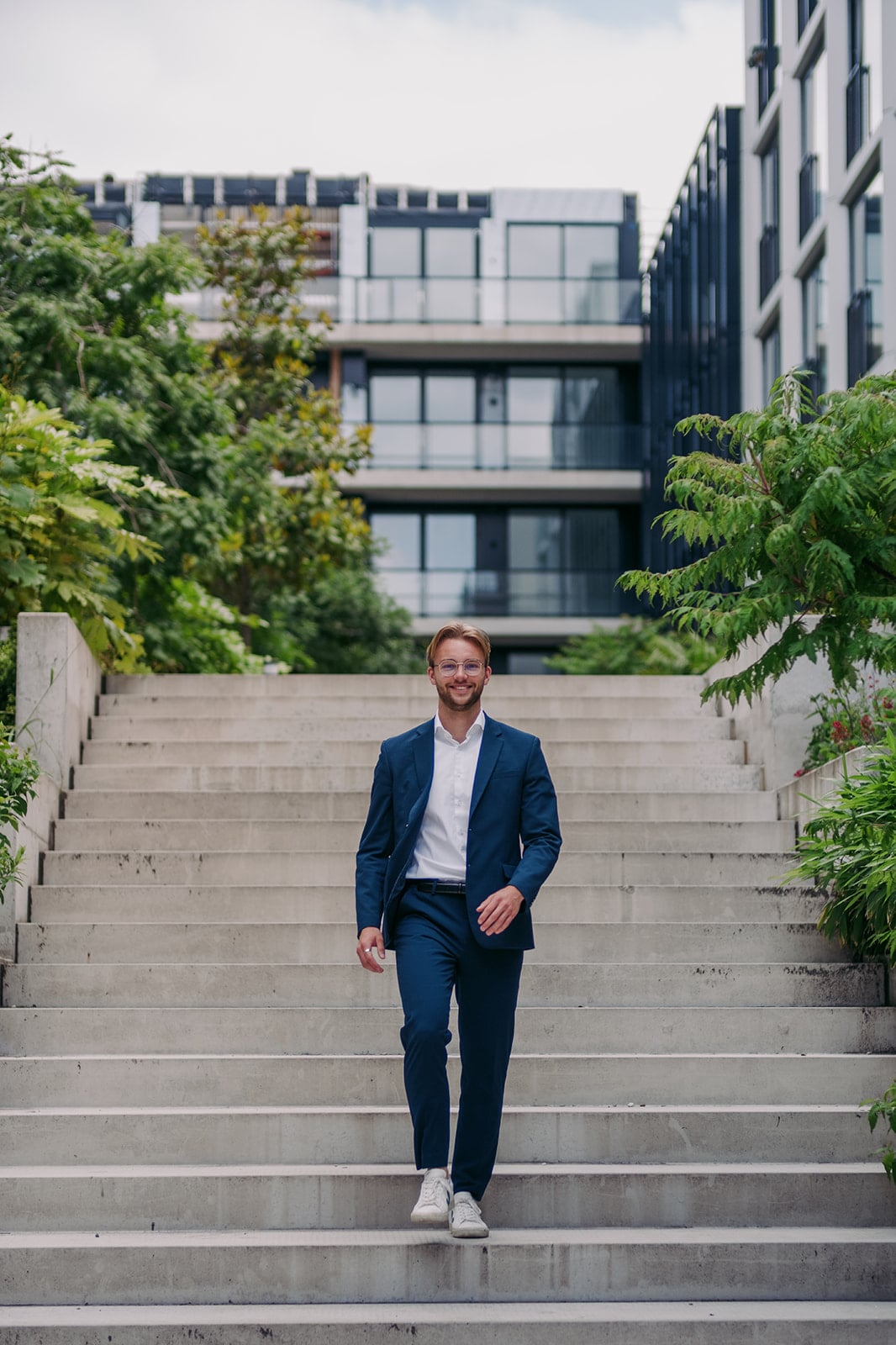 Lachende man blauw pak witte sneakers betonnen trap bedrijfsfotografie Utrecht regio Nederland