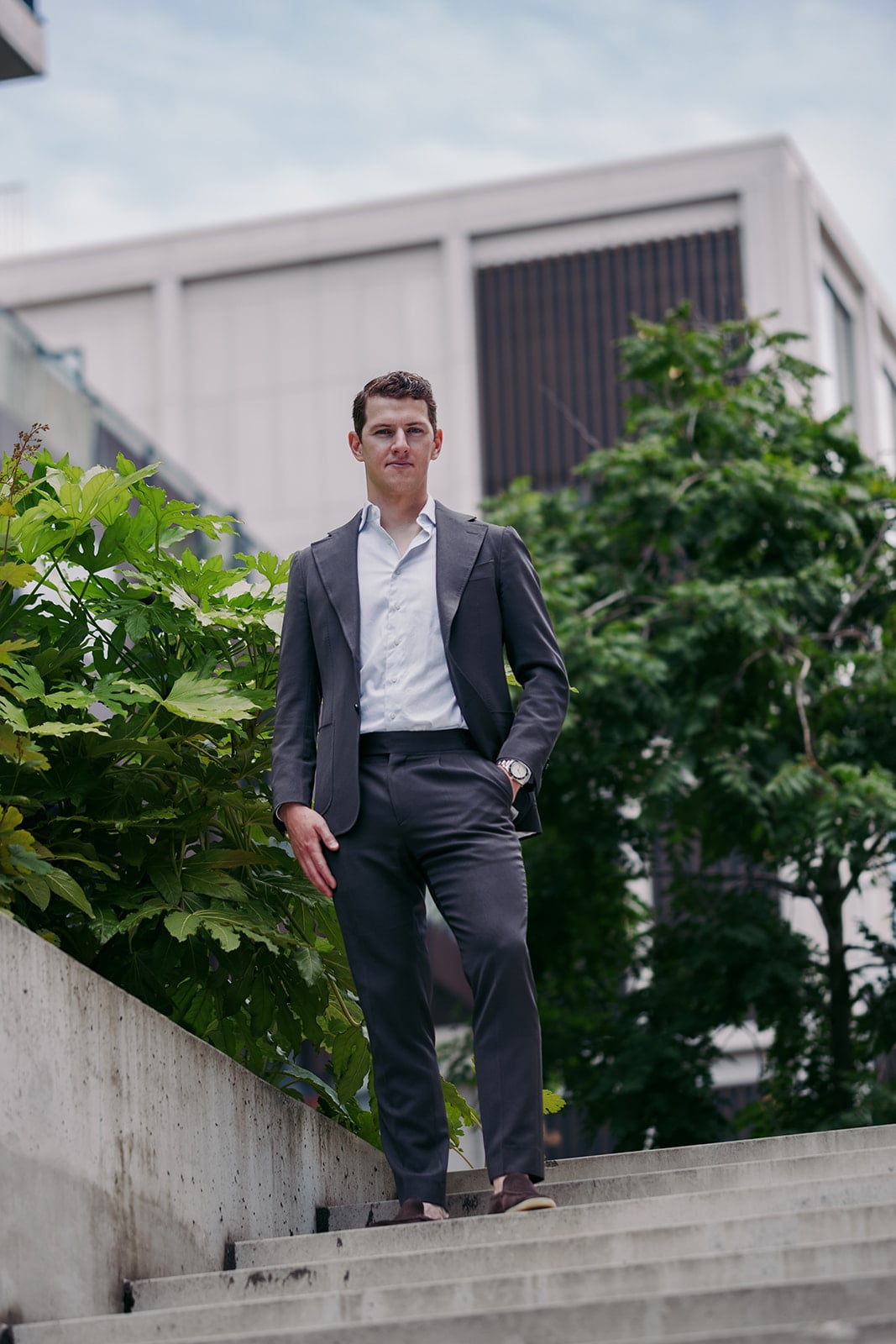 Zakenman grijs pak wit overhemd horloge betonnen trap groene beplanting corporate portret